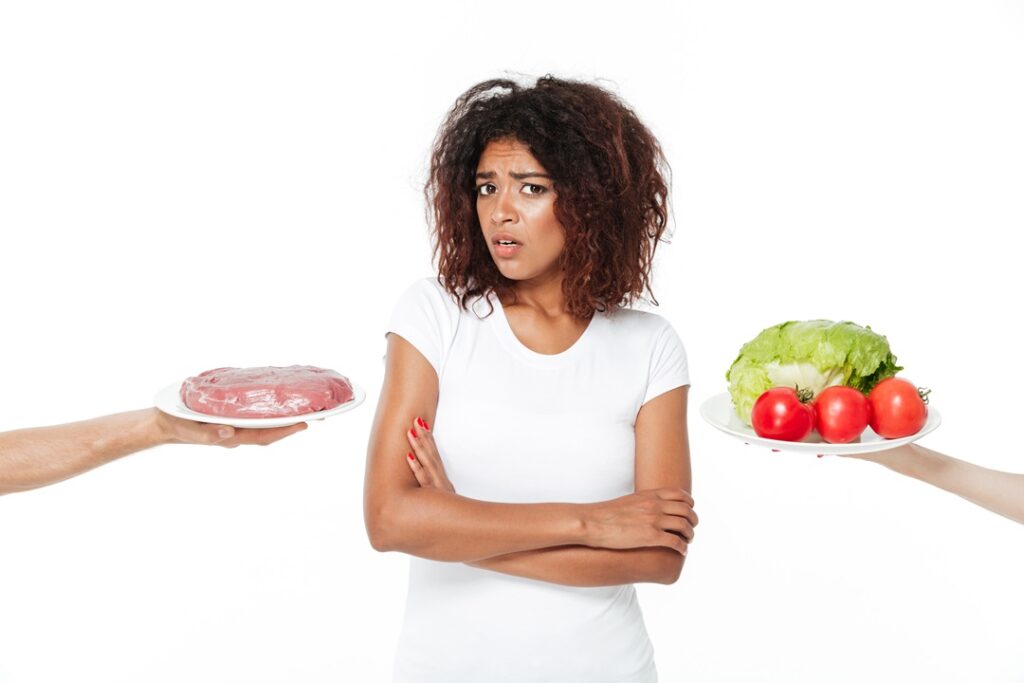 The Importance of Reasonable Adjustments confused young african woman choosing between meat and vegetables.