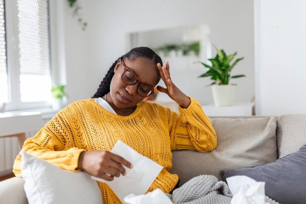 portrait of an attractive woman sitting on a sofa at home with a headache, feeling pain and with an expression of being unwell. upset depressed woman lying on couch feeling strong headache migraine.