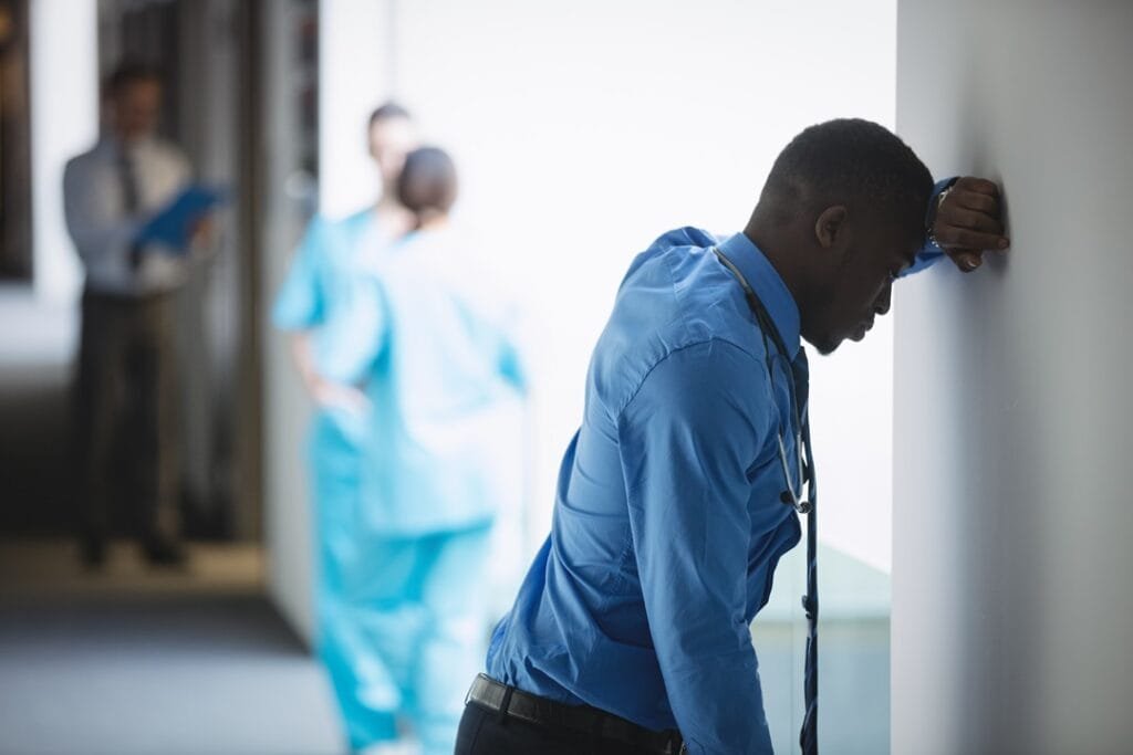 sad doctor leaning on wall in hospital corridor